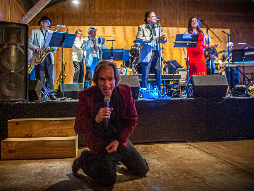 A singer kneeling near a stage with people on the stage behind him